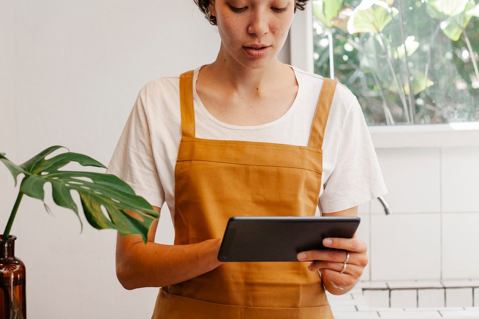 Café worker in an apron reviewing information on a tablet at the counter