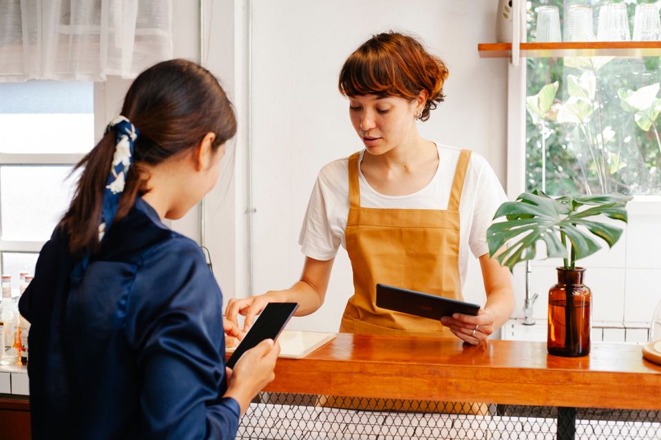 Two café workers discussing a smartphone and tablet at the counter