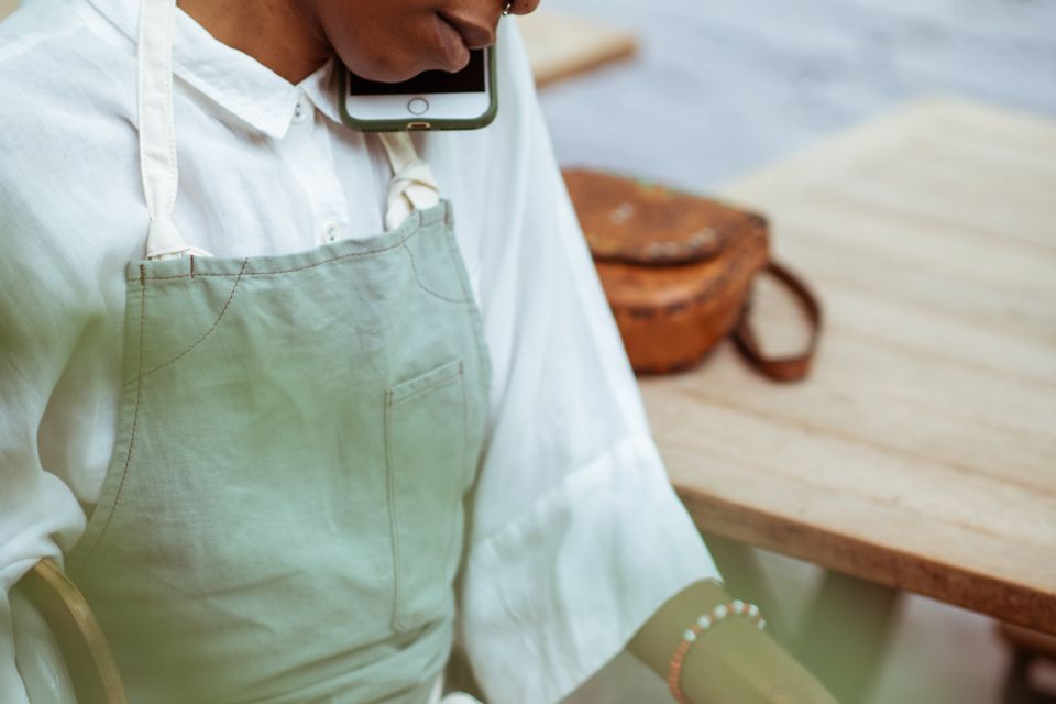 Café worker in an apron speaking on a phone beside a work table