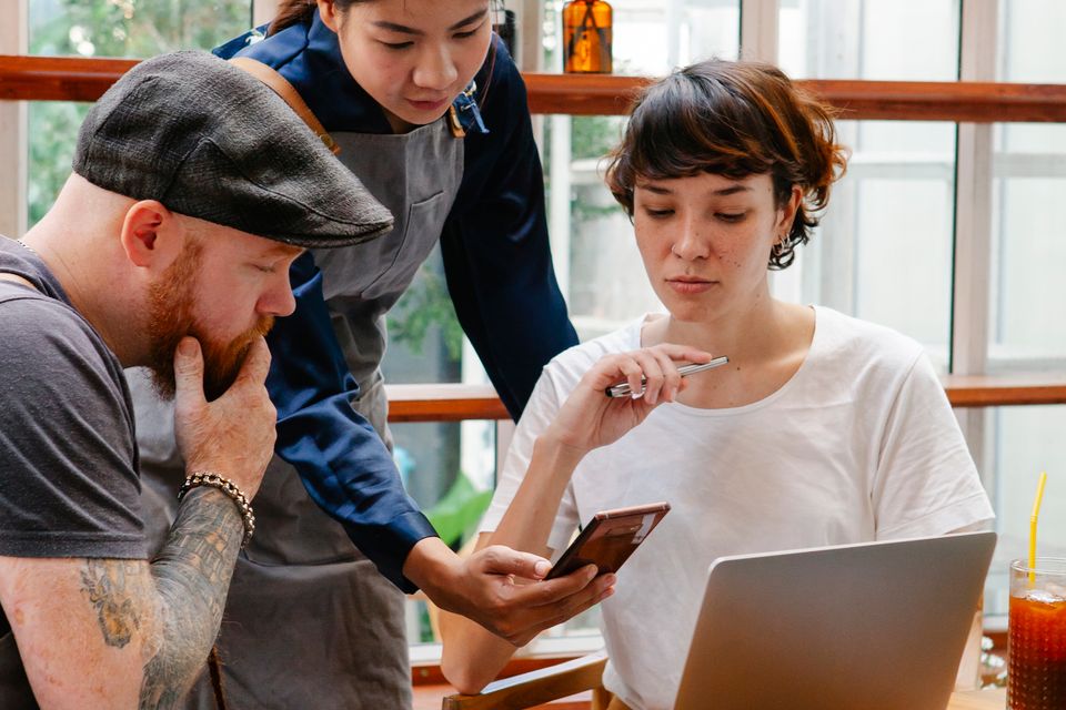 Café coworkers discussing information on a smartphone beside a laptop