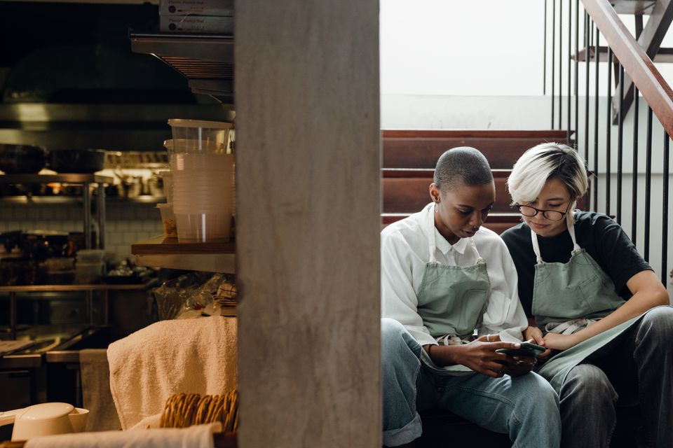 Two café workers resting together and looking at a smartphone