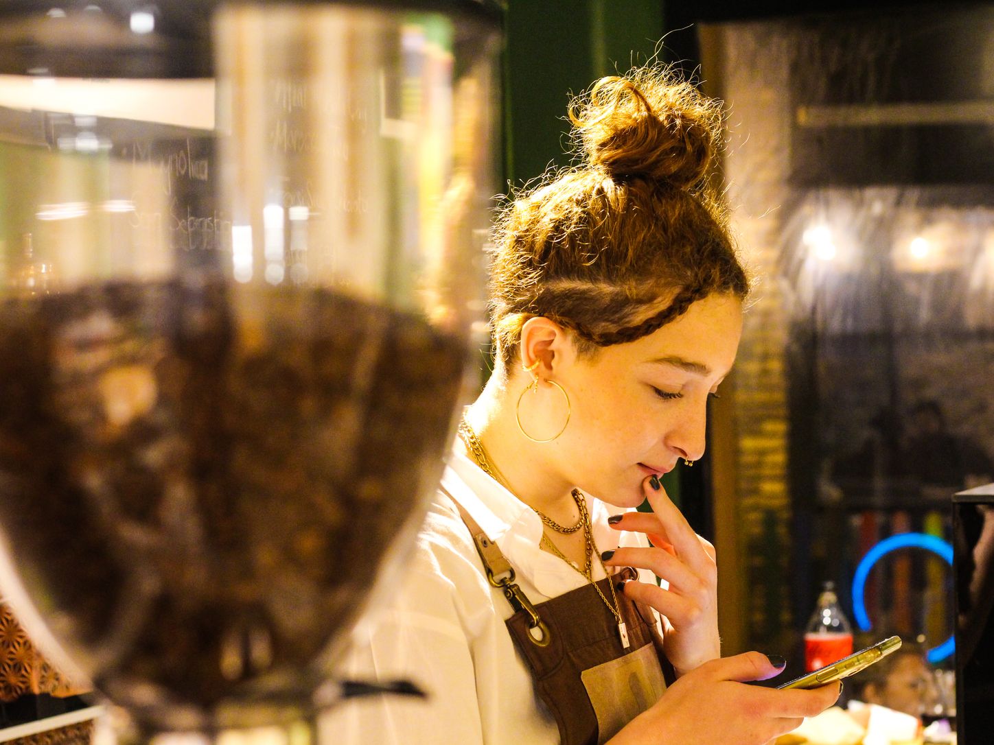 Barista in an apron looking at a smartphone in a cafe